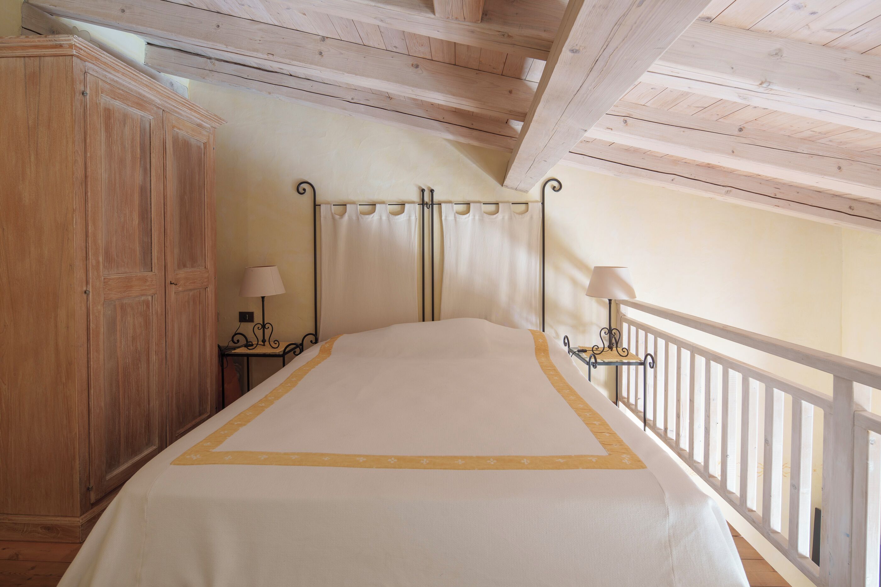 Een slaapkamer met een bed, een houten garderobe, twee nachtkastjes en een witte balustrade.