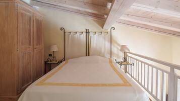 Een slaapkamer met een bed, een houten garderobe, twee nachtkastjes en een witte balustrade.