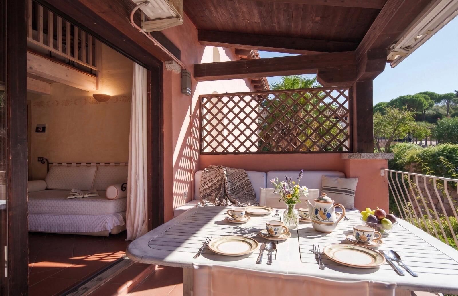 Patio soleggiato con tavolo da pranzo per due persone, una panca imbottita e vista su piante.