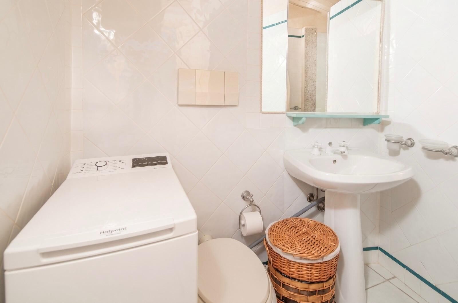 A bathroom with a washing machine, a sink, a toilet, and a wicker basket.