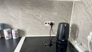 Una cocina con un fogón de inducción negro, una cafetera negra y dos recipientes blancos con diseños florales.