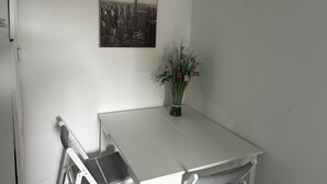 Una mesa blanca con una fotografía en blanco y negro de un paisaje urbano sobre ella, un jarrón con flores y una silla.