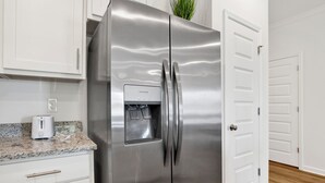 A stainless steel refrigerator with a water dispenser, white cabinets, and a wooden floor. - Brand New 3-bedroom townhome with AC in the heart of Orange Beach (Orange Beach)