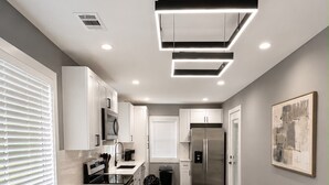 A modern kitchen with white cabinetry, a central island with bar stools, a stainless steel refrigerator, and a contemporary light fixture.