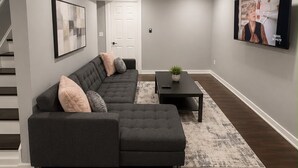A modern living room with a sectional sofa, a coffee table, and a flat-screen TV mounted on the wall.
