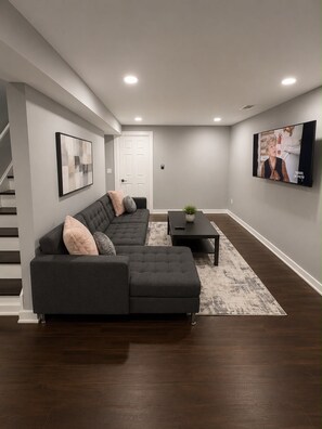 A modern living room with a sectional sofa, a coffee table, and a flat-screen TV mounted on the wall. - Cozy Modern Escape Near Downtown ATL (Atlanta)