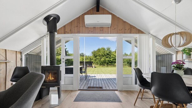 En modern inredning med en vedeldad kamin, en matplats med stolar och utsikt över en terrass och en trädgård.