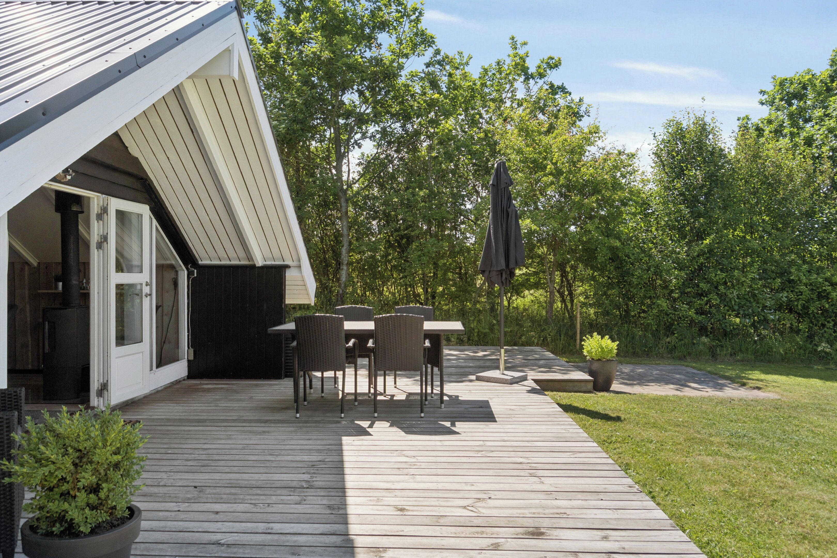 Een houten terras met buitenmeubilair, een overdekte zithoek en uitzicht op een weelderig groen landschap.