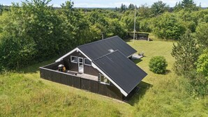 Ett modernt hus med ett sluttande tak, omgivet av frodig grönska och en klar himmel.