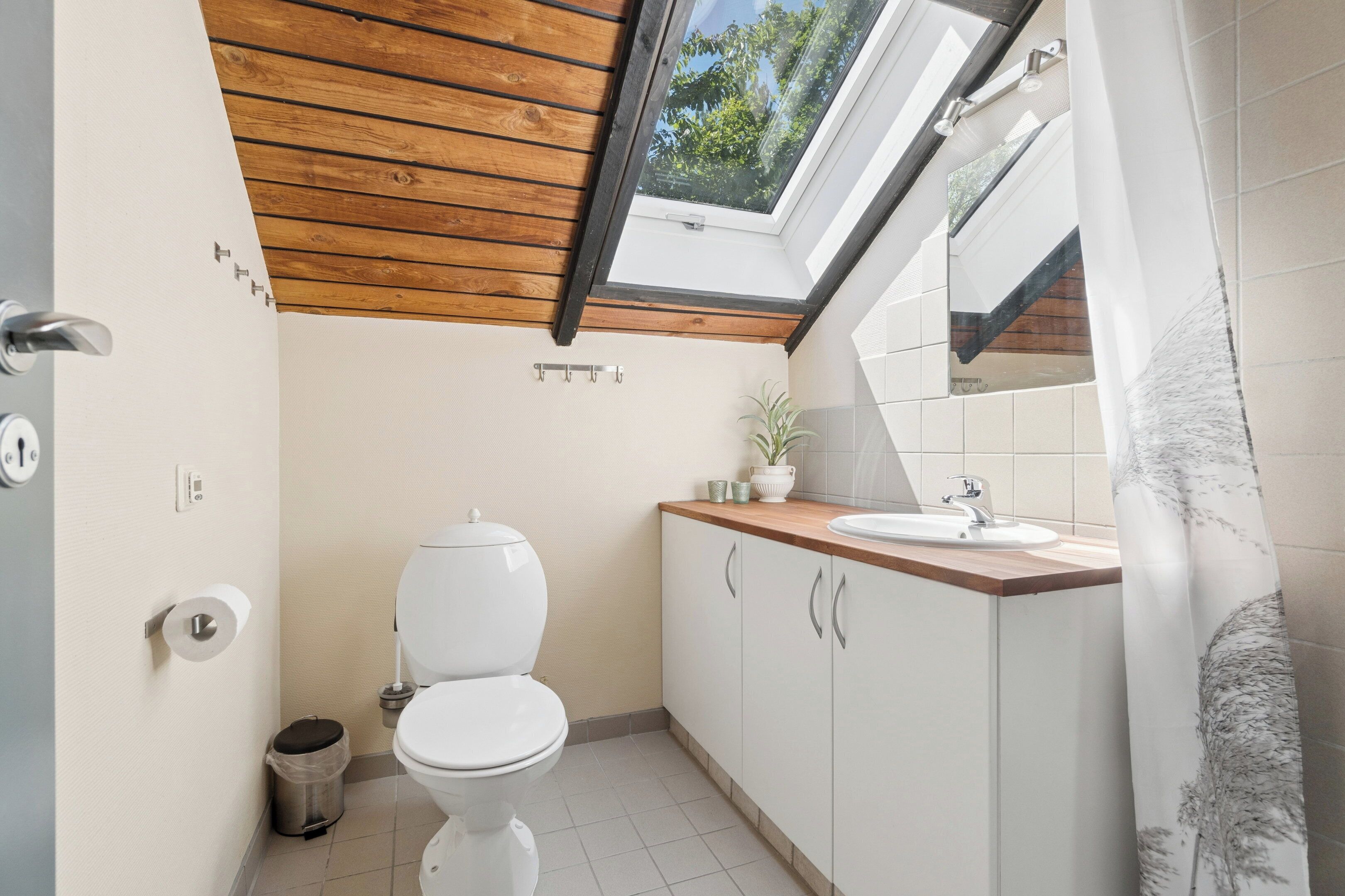 A modern bathroom with a skylight, white toilet, wooden ceiling, and a sink with a mirror above it.