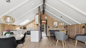 Ett modernt kök i loftstil med trädetaljer, en matplats med svarta stolar och en mysig sittgrupp med en grå soffa.