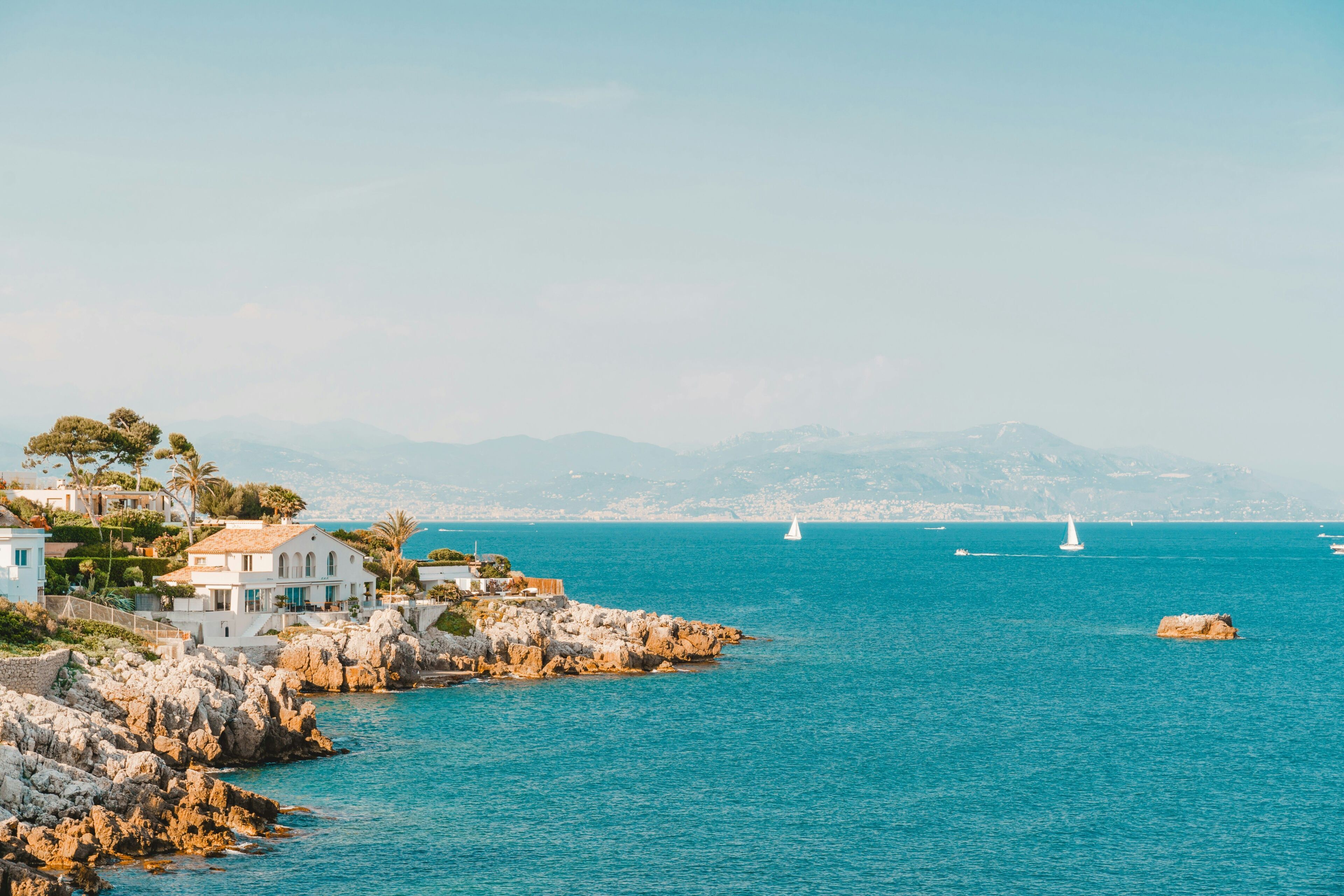 A coastal town with rocky shores, white buildings, and sailboats on the sea.