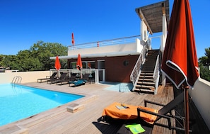 Zona de piscina amb gandules, un pont de fusta i una escala que condueix a una coberta superior.