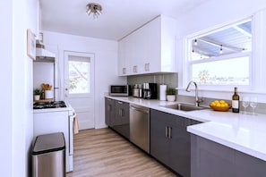 A modern kitchen with white cabinets, stainless steel appliances, and a window with a view. - CasaViva Vista · Top-Floor 2BR with Private Porch, City Views, Walk to Eats (San Diego)
