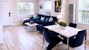 A modern living room with a sofa, coffee table, and dining table. - CasaViva Breeze 2BR w/ Sunset Views, Firepit & Backyard — Walk to Fun & Eats (San Diego)
