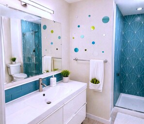 Ein modernes Badezimmer mit einem weißen Waschtisch, einem großen Spiegel, einer Dusche mit geometrischem Fliesendesign und einer Wand mit kreisförmigen und sternförmigen Verzierungen.