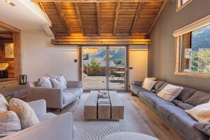 Un salon moderne avec un plafond en bois, un ensemble de canapés, une table basse et une vue sur une terrasse extérieure, accessible par une porte vitrée.