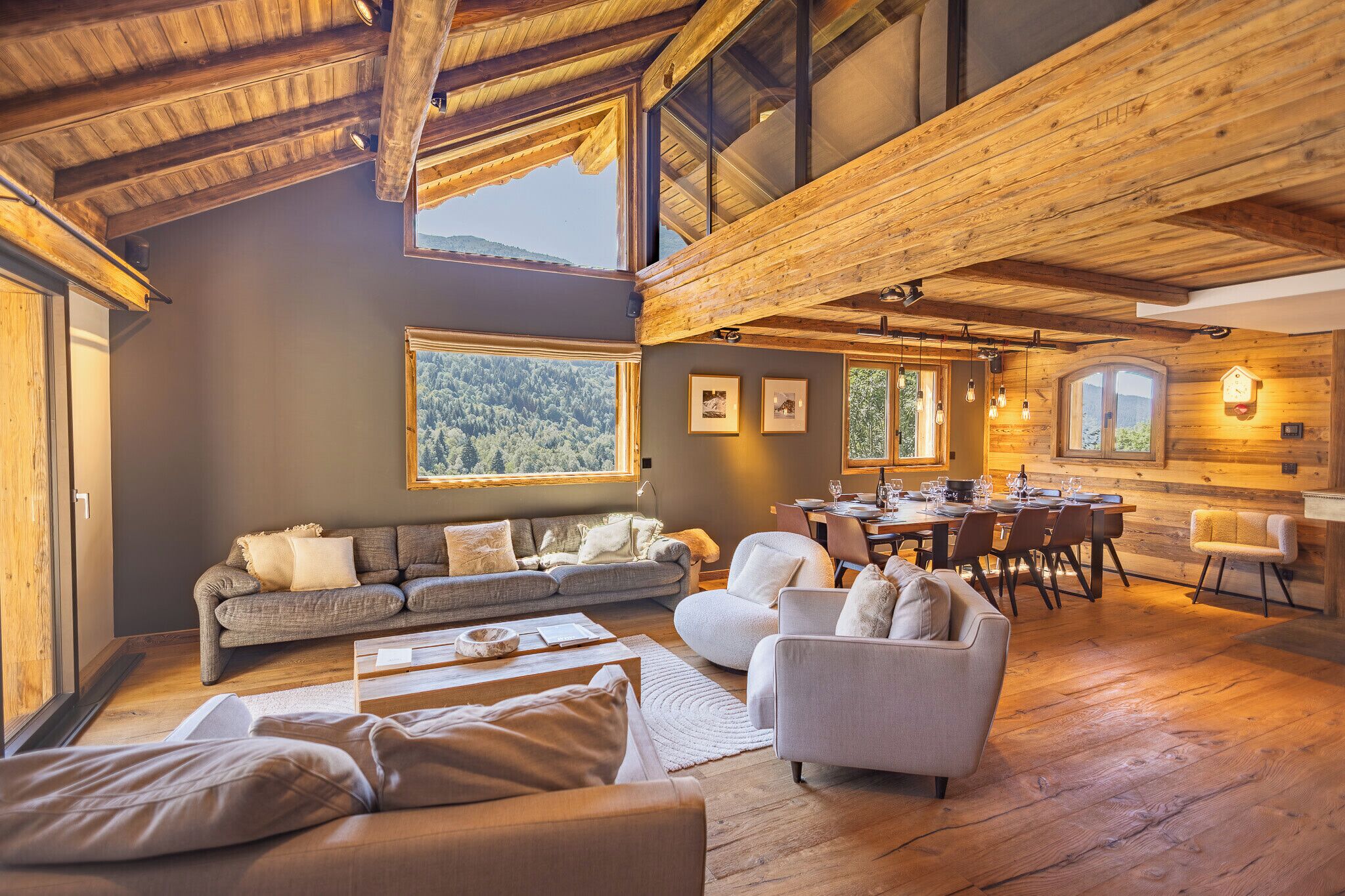A spacious living area with a high ceiling, wooden beams, a gray sofa, a dining table with chairs, and a view of the outdoors.