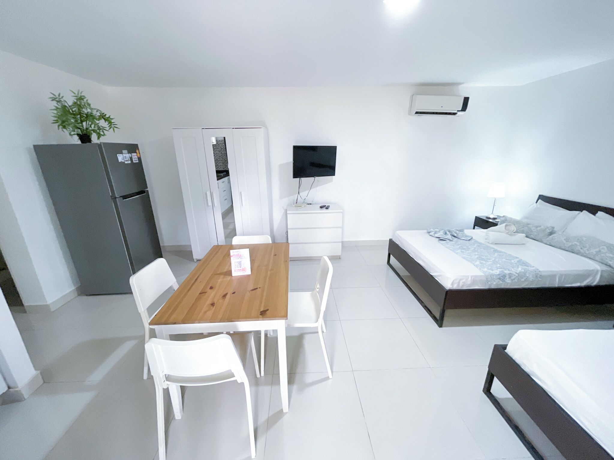 Un dormitorio con cama, televisor, escritorio con silla, refrigerador y armario.