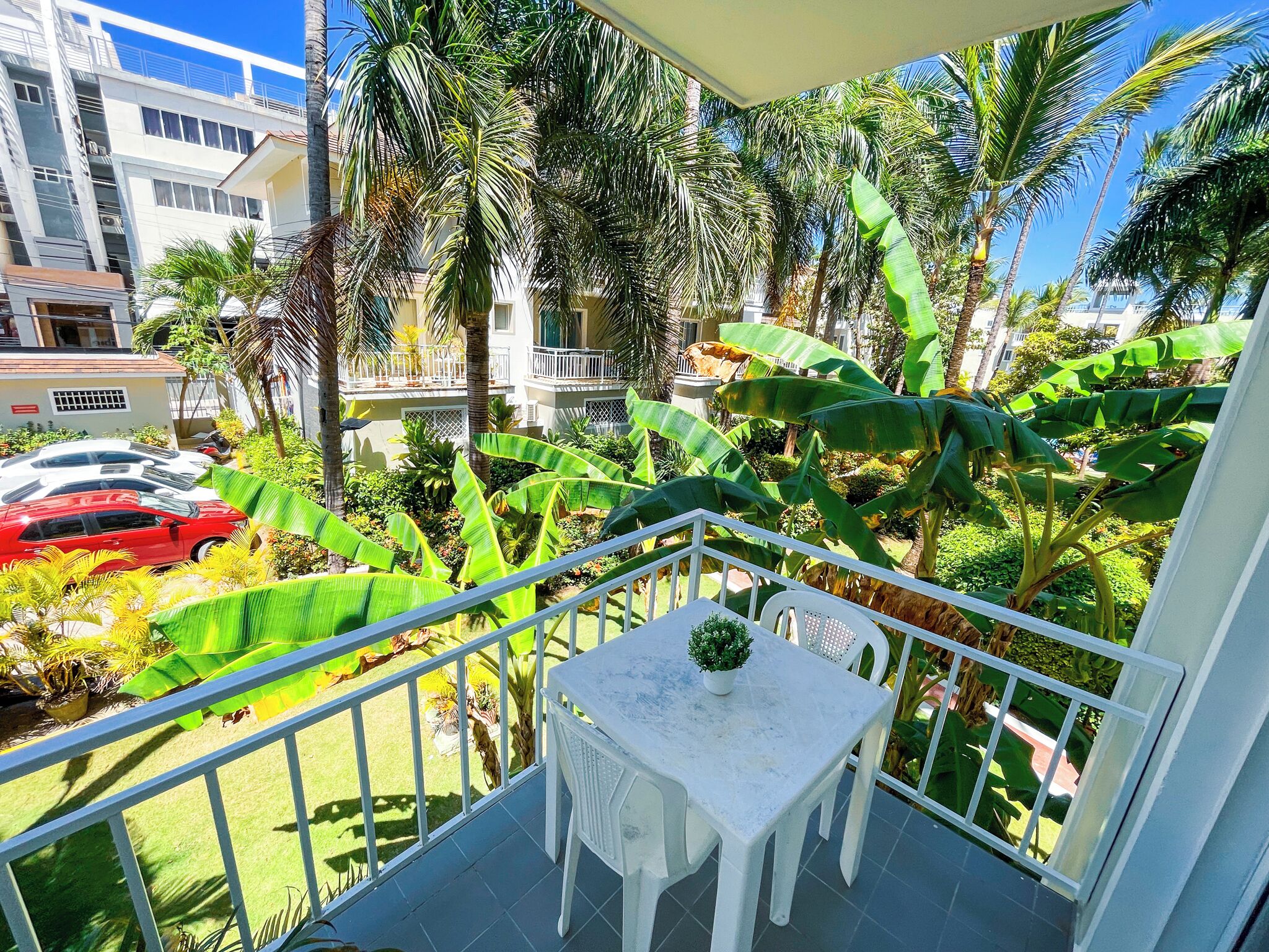 Ein Balkon mit weißem Tisch und Stühlen, umgeben von üppiger Vegetation und Bananenpflanzen.