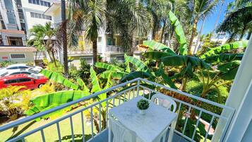 Ein Balkon mit weißem Tisch und Stühlen, umgeben von üppiger Vegetation und Bananenpflanzen.
