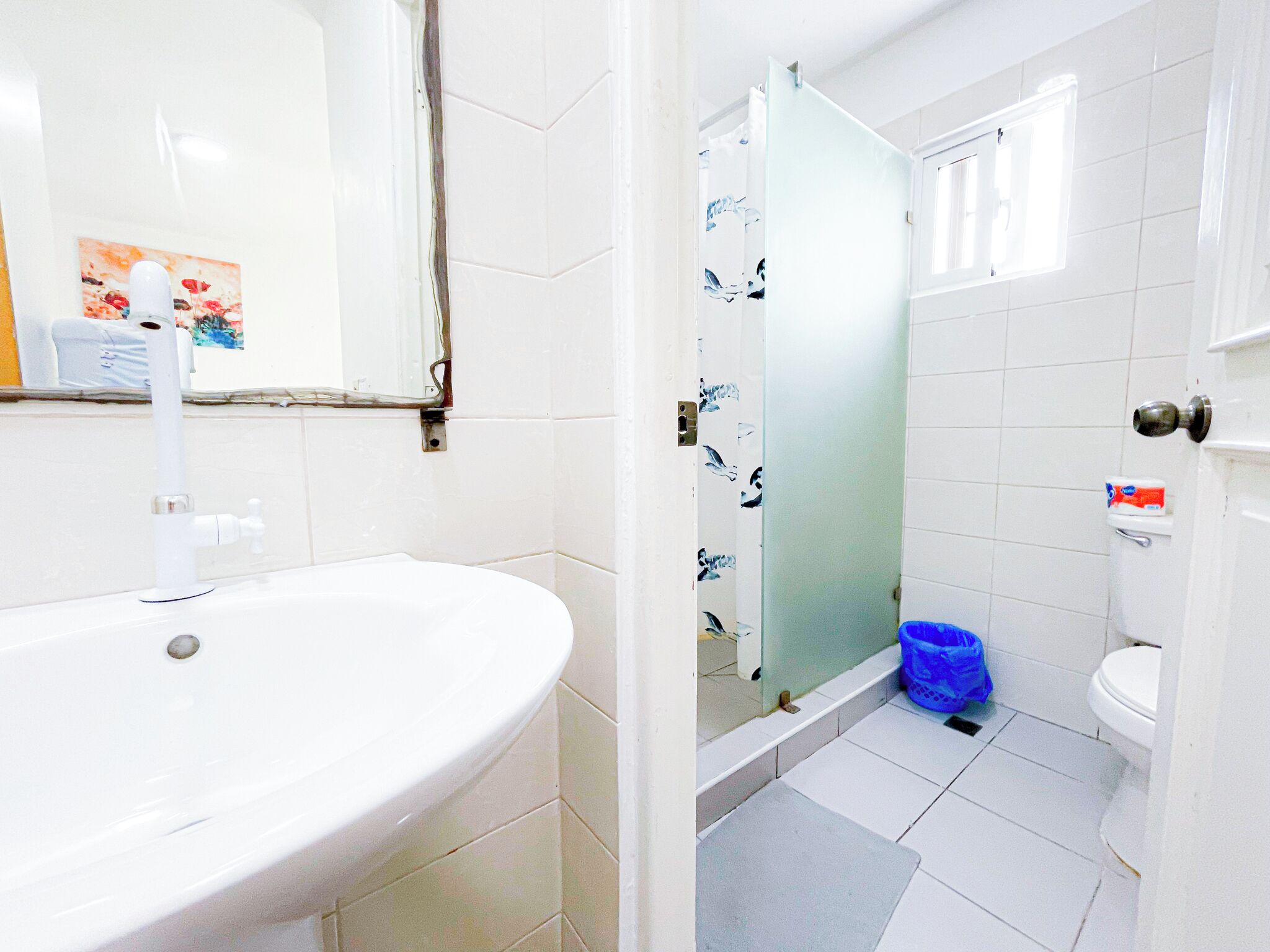 Ein Badezimmer mit Waschbecken, Toilette, Dusche und einem blauen Mülleimer.
