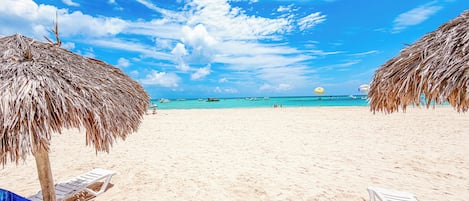Een strand met rieten parasols, een helderblauwe lucht en een rustige zee.