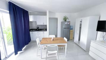 A modern kitchen with white cabinets, a wooden dining table, and a refrigerator.