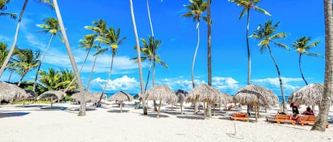 A beach with palm trees and thatched umbrellas.