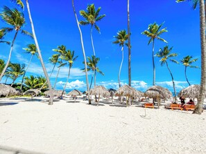 A beach with palm trees and thatched umbrellas. - TROPICANA Sol Caribes STUDIOS HOTEL (Punta Cana)