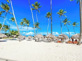 A beach with palm trees and thatched umbrellas.
