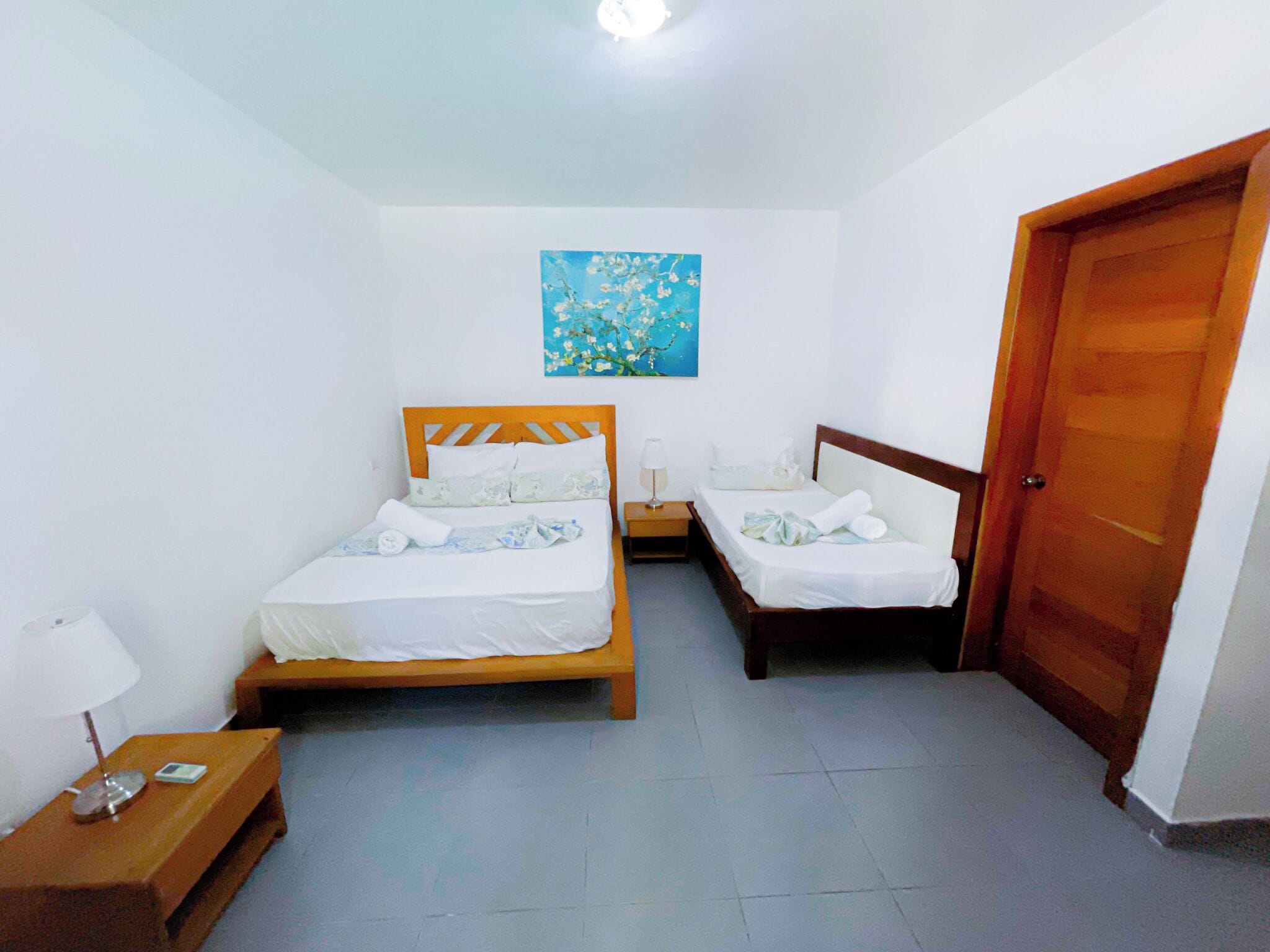 Una stanza con due letti, una porta in legno, un comodino con una lampada e un quadro appeso al muro.