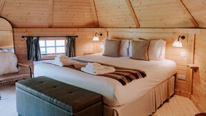 A wooden cabin bedroom with a bed, nightstands, a bench, and a window with curtains.