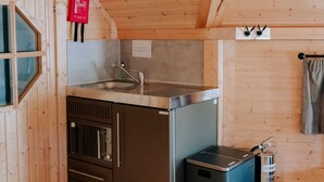 A compact kitchen with wooden walls, a stainless steel sink, a microwave, and a small trash bin.