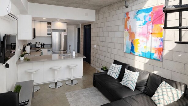 Un espacio habitable moderno con un sofá de cuero negro, una zona de cocina y un cuadro abstracto grande en la pared.