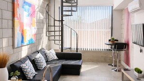 Una cocina moderna con un lavaplatos empotrado, una escalera y una zona de estar con un sofá negro y un cuadro abstracto colorido.