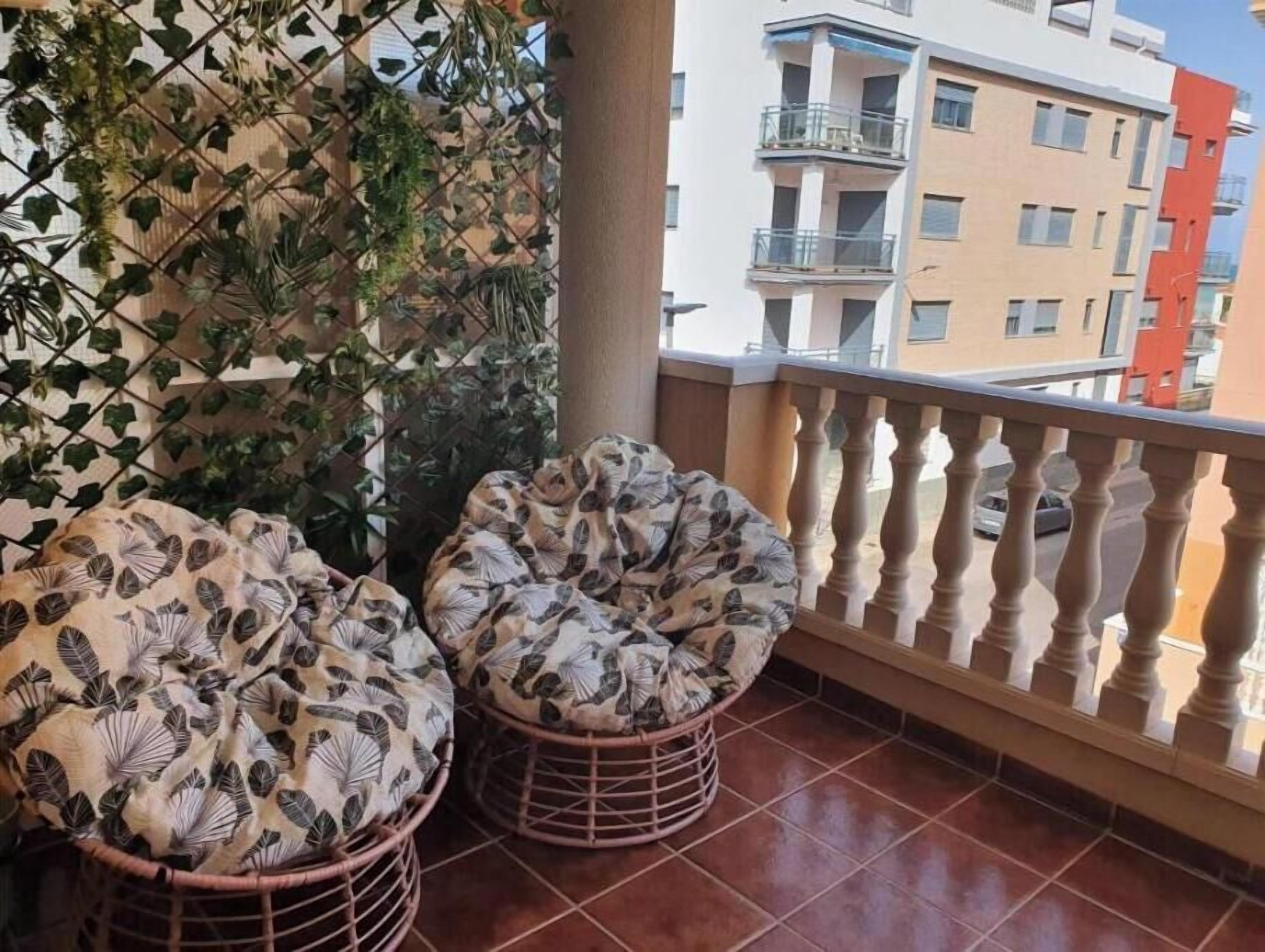 A balcony with two cushioned chairs, a decorative wall, and a view of adjacent buildings.