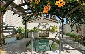 Ein überdachter Außenpool mit einer Pergola, Treppen zum Pool und umgebender Bepflanzung.