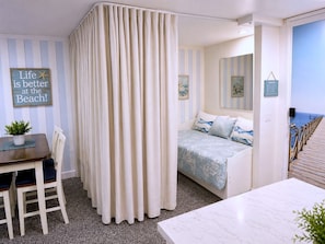 Ein Zimmer mit einem Bett, einem Esstisch, Stühlen, einem Vorhang, einem Schild und Blick aufs Meer.