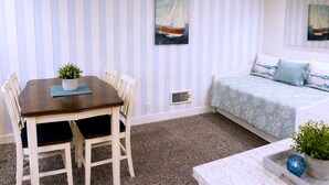 Une pièce comprenant une table à manger, des chaises, un ventilateur de plafond, un lit recouvert d’une couvre-lit à motifs et deux tableaux accrochés au mur.