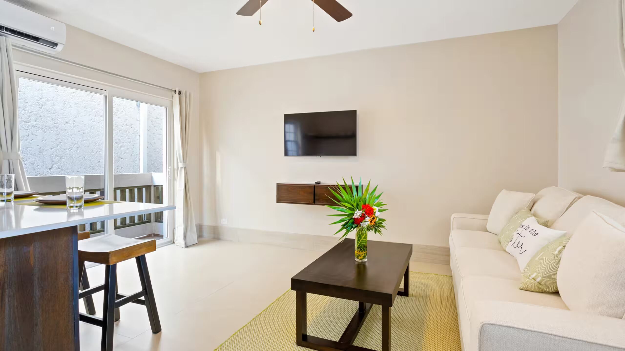 Un salon moderne comprenant un canapé, une table basse, un téléviseur fixé au mur et un coin repas avec une table et des chaises.