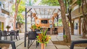 Un área de patio al aire libre con barra de madera, asientos y una pantalla de televisión.