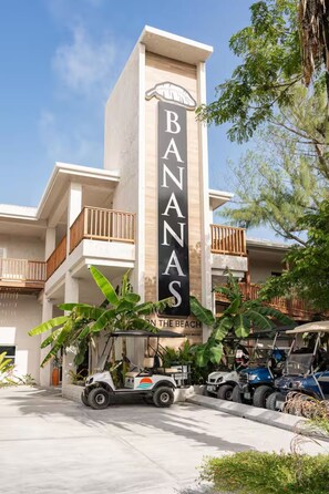 A building with a vertical sign reading 'BANANAS' and a sign below stating 'ON THE BEACH.' There are vehicles parked in front, and the building has balconies.