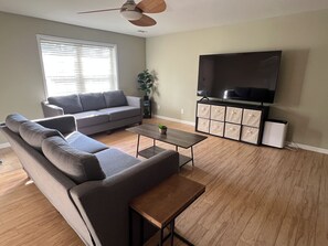 A living room with a sofa, coffee table, and a flat-screen TV mounted on the wall.