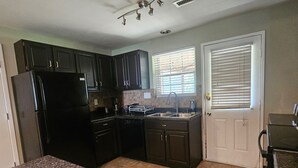 Keittiössä on tummat kaapit, musta jääkaappi, astianpesukone, pesuallas ja ikkuna, jossa on sälekaihtimet.