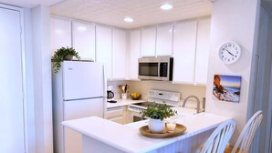 A modern kitchen with white cabinetry, a central island, a microwave, a stove, and a clock on the wall. - SolMar Vista 2BR/2BA Oceanview, Heated Pools, Hot Tubs & Steps to Beach (Oceanside)