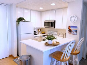 A modern kitchen with white cabinetry, a central island, a microwave, a stove, and a clock on the wall. - SolMar Vista 2BR/2BA Oceanview, Heated Pools, Hot Tubs & Steps to Beach (Oceanside)