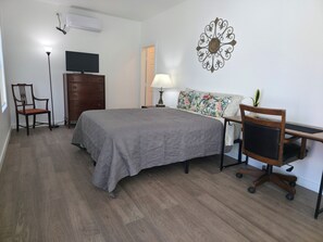 Ein Schlafzimmer mit Bett, Kommode, Stuhl, Schreibtisch, Lampe und Wanddekoration.