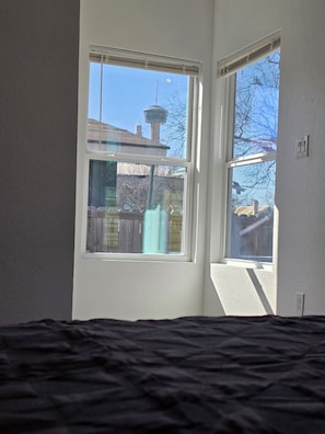 Ein Zimmer mit einem Bett, zwei Fenstern und Blick auf ein Gebäude mit einem Turm.