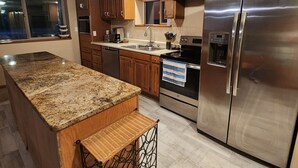 A kitchen with granite countertops, wooden cabinets, stainless steel appliances, and a window.